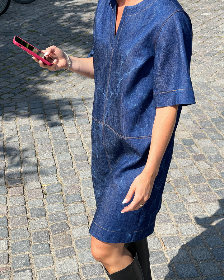 Person wearing a blue denim dress on a cobblestone street.