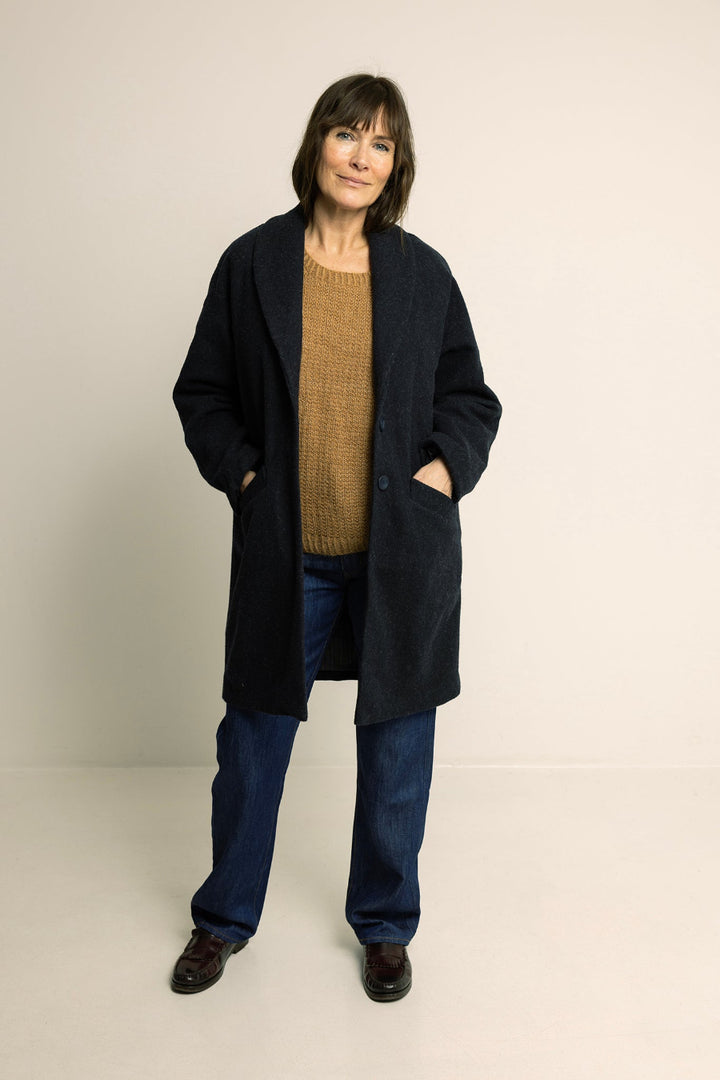 Person wearing a black coat, brown sweater, and blue jeans on a plain background