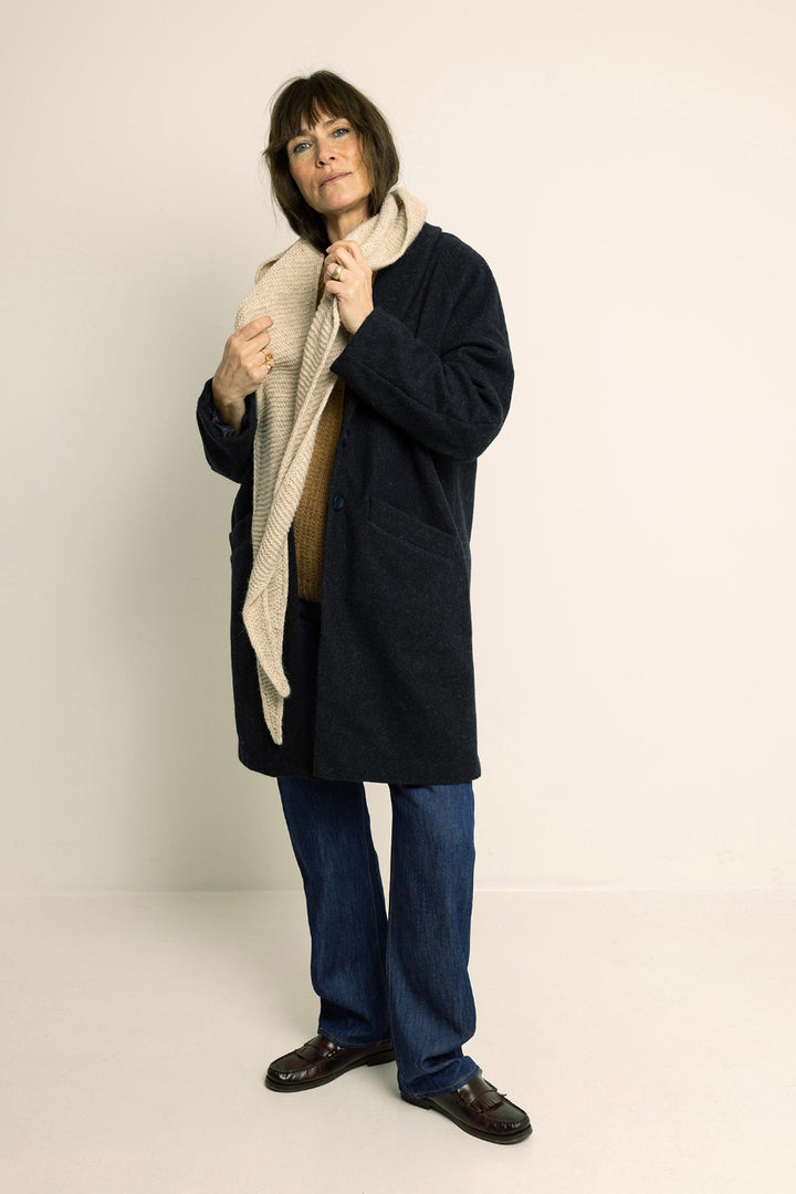Person wearing a dark coat and blue jeans holding a beige scarf against a white background