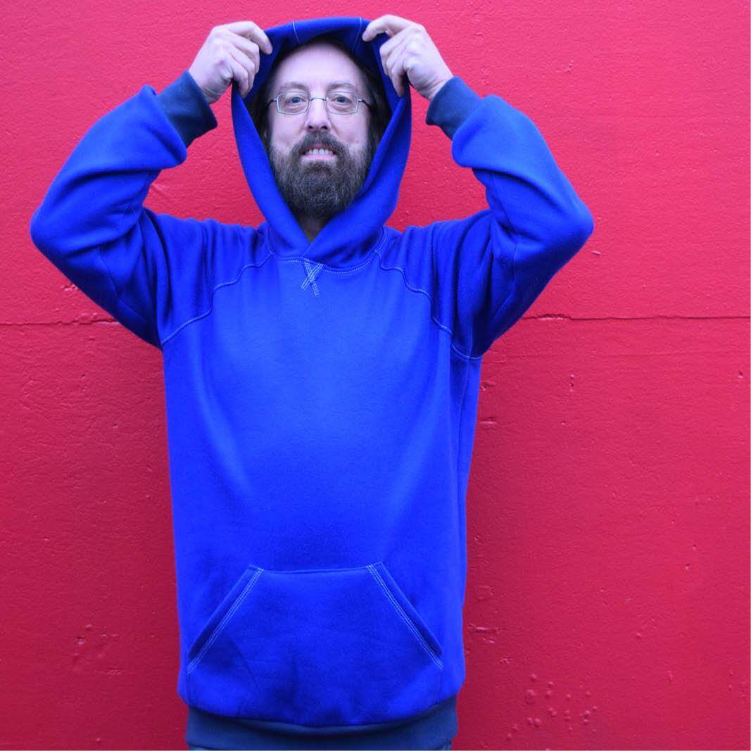 Man wearing a blue Rebel raglan sweater with a hood against a red background.