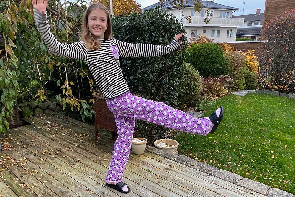 Girl wearing colorful pajama pants demonstrating how to sew pajama pants for everyone in your family.