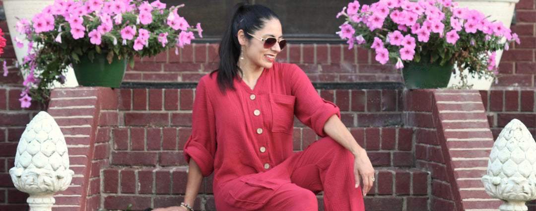 Woman wearing a red jumpsuit sewing pattern with flowers in the background, showcasing the Avivator jumpsuit style.