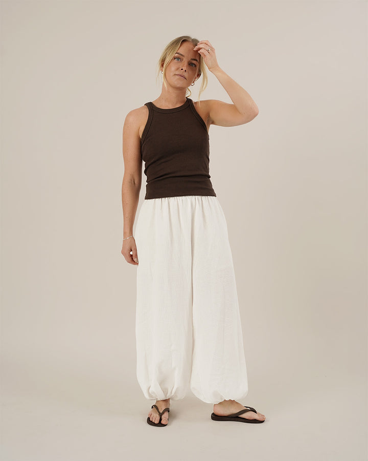 Woman wearing a brown tank top and white pants against a beige background
