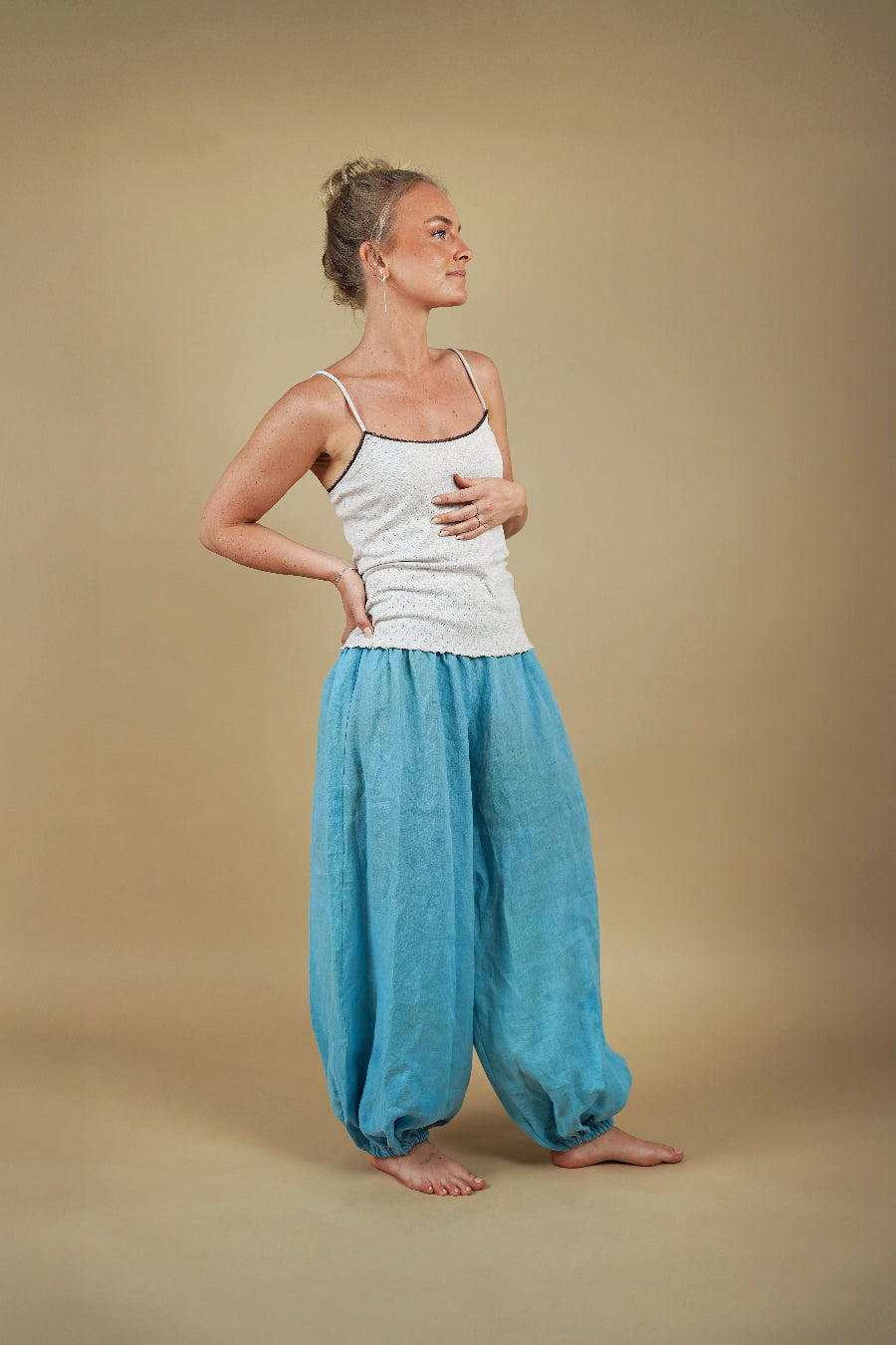 Woman wearing a white tank top and blue harem pants against a beige background