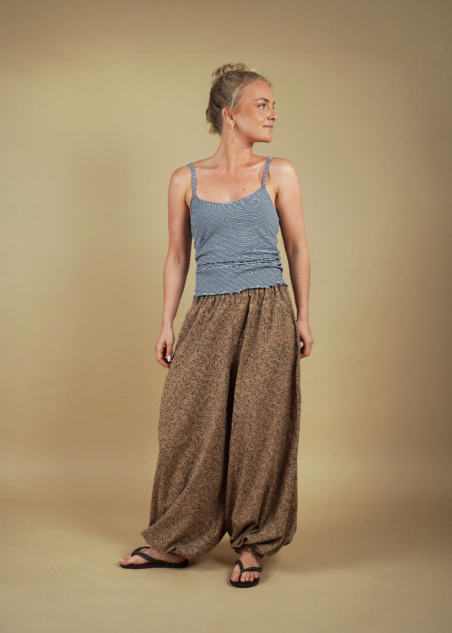 Woman wearing a blue tank top and brown wide-leg pants against a beige background