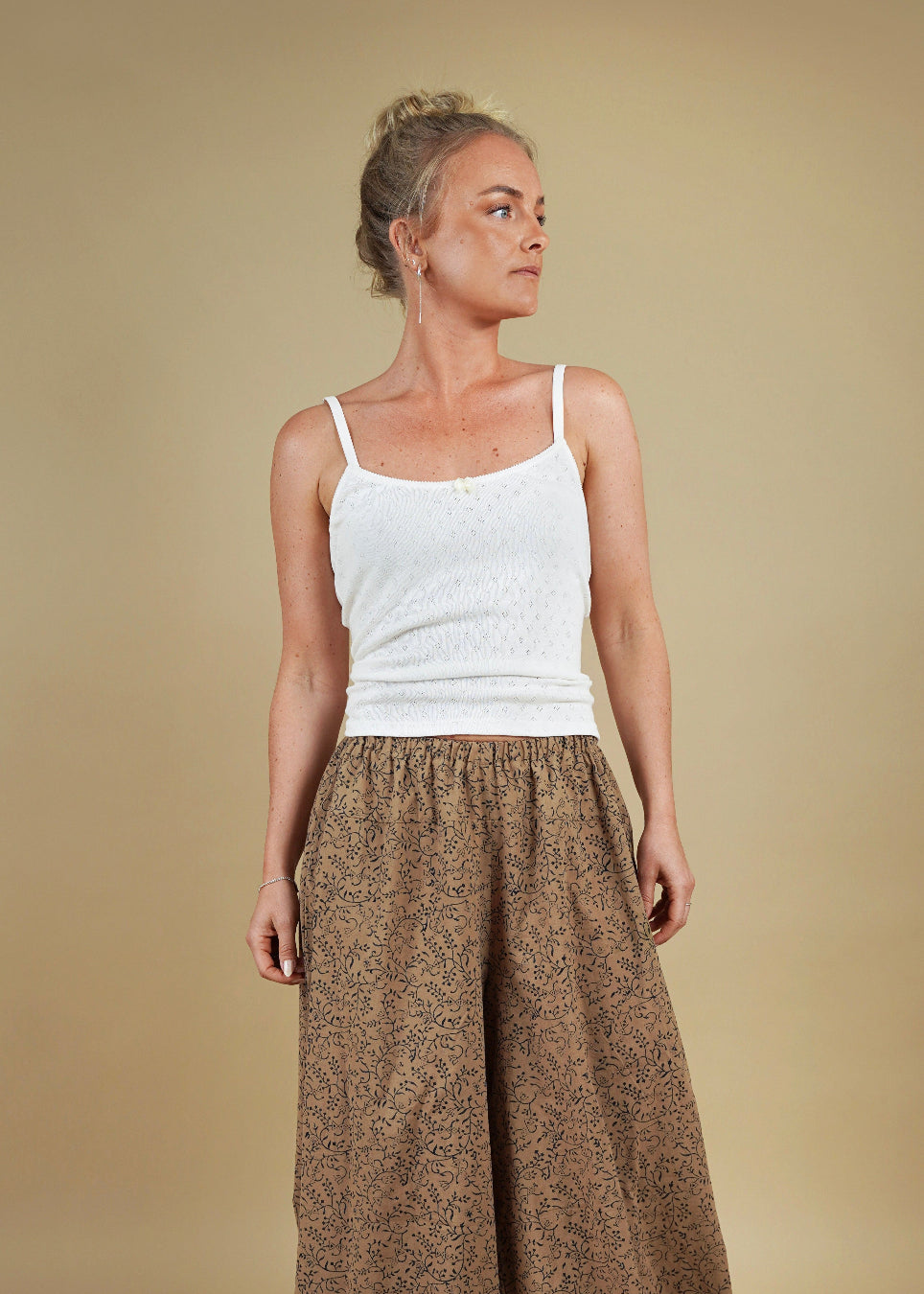 Woman wearing a white tank top and brown patterned pants on a beige background