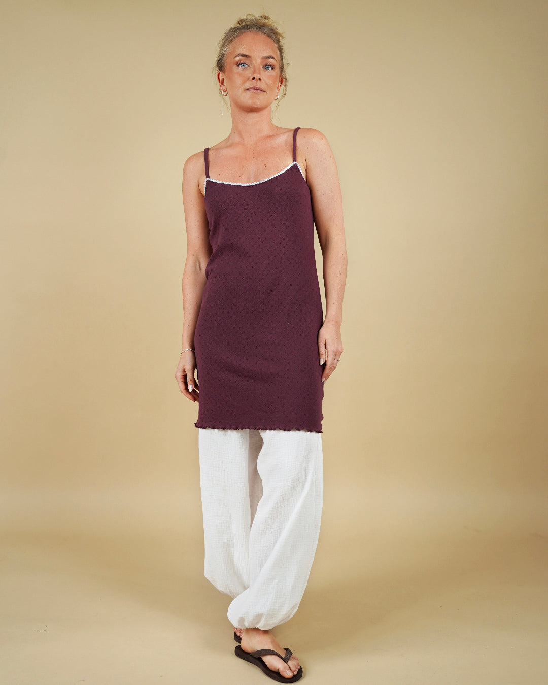Woman wearing a purple slip dress and white pants against a beige background