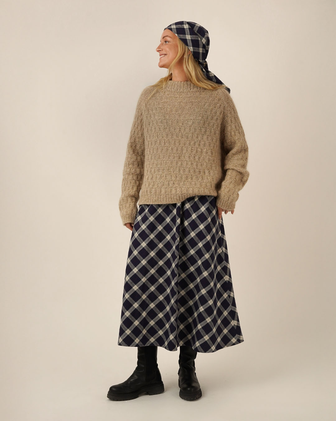Person wearing a beige sweater and Claude skirt sewing pattern with a headscarf on a plain background