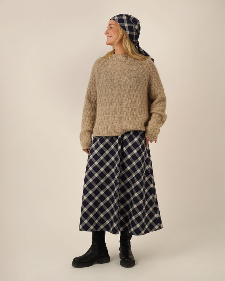 Person wearing a beige sweater and Claude skirt sewing pattern with a headscarf on a plain background