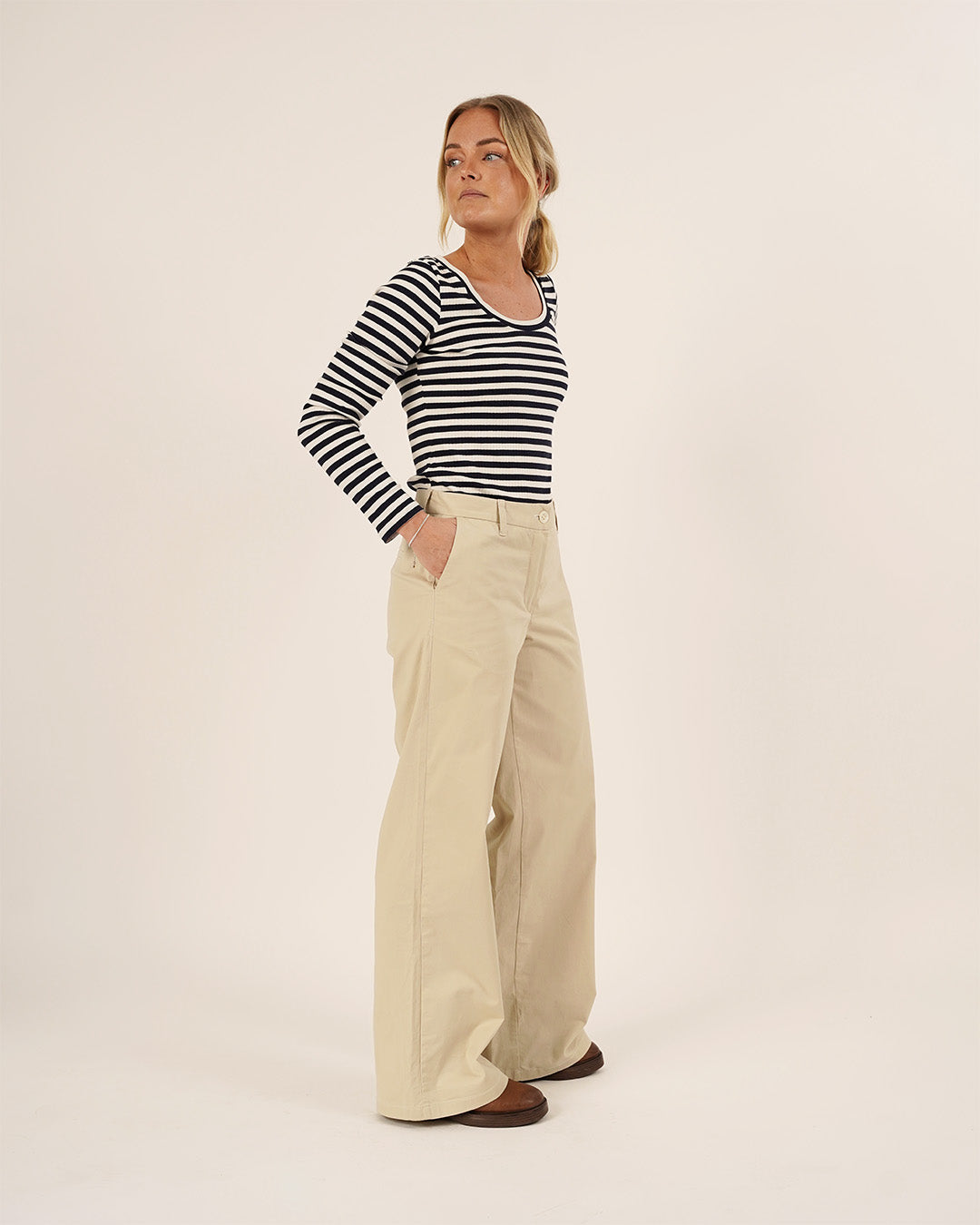 Woman wearing a striped shirt and beige pants on a white background