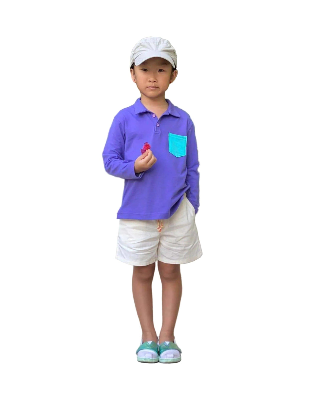 Child wearing a purple polo shirt, white shorts, and a cap in a garden, showcasing the Kids Pants & Shorts Sewing Pattern.