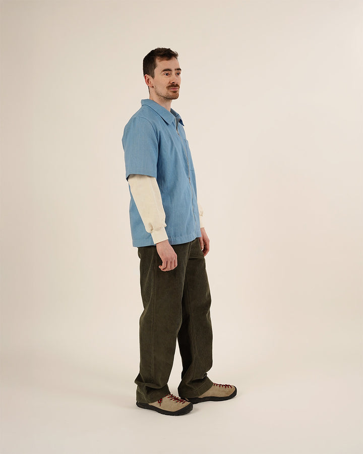 Man wearing a blue shirt with a white sleeve and brown pants on a beige background