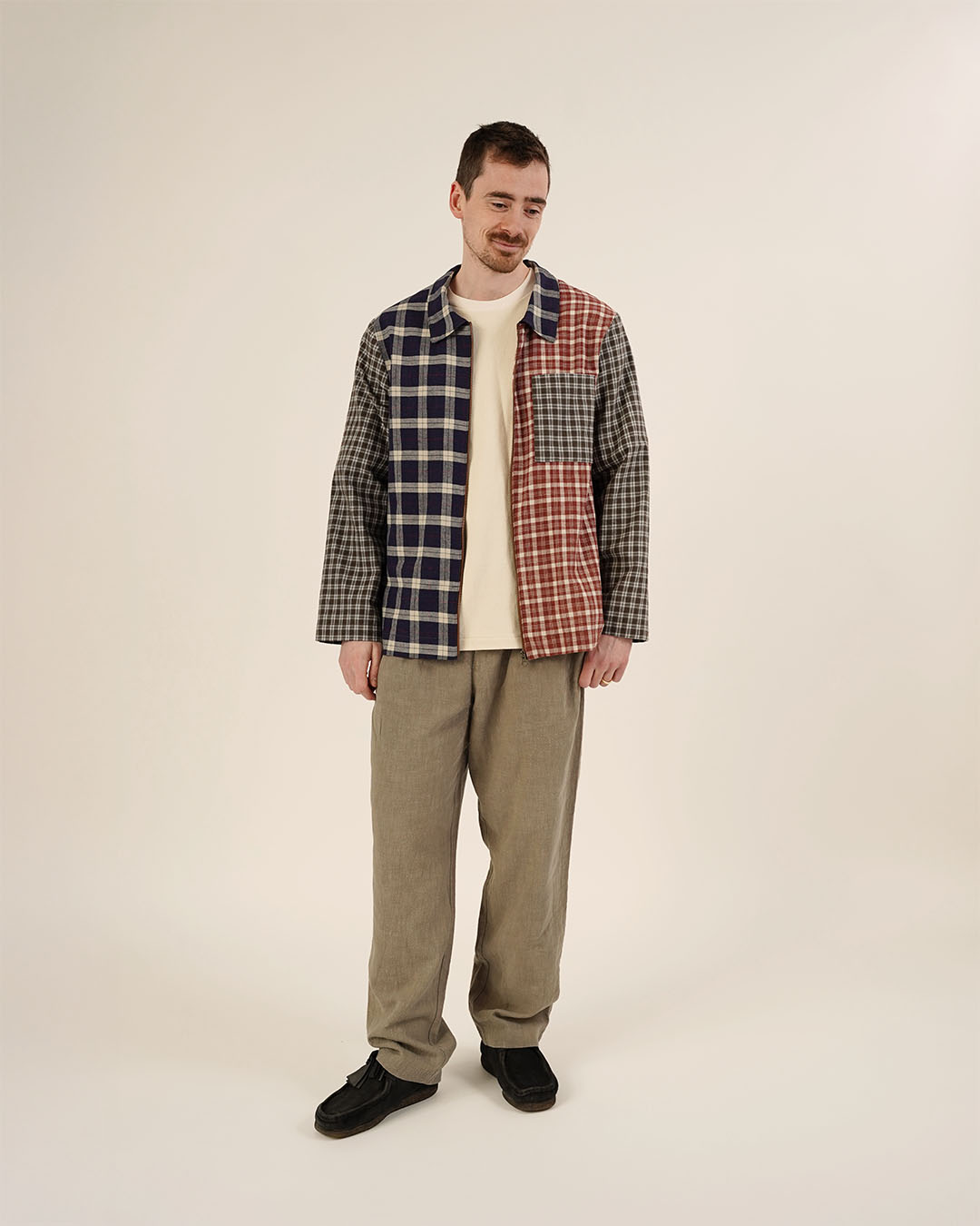 Person wearing a patchwork jacket with plaid patterns on a plain background