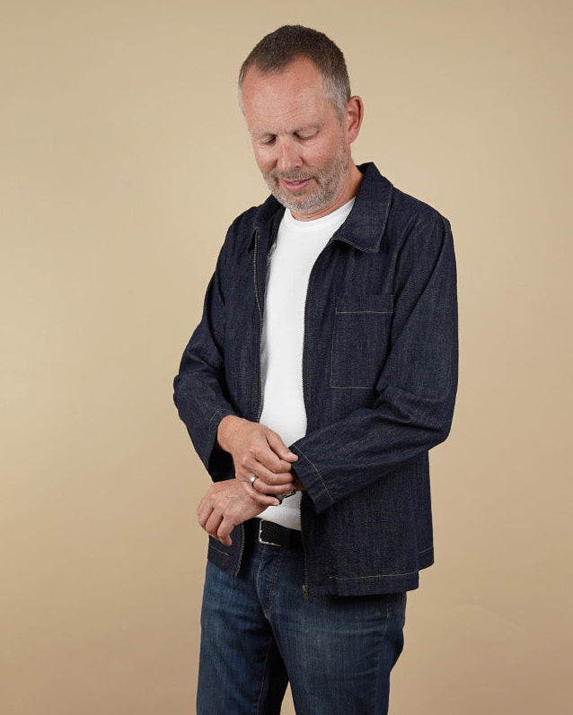 Man wearing a men's zip zhirt sewing pattern white shirt, blue jeans, and blue shoes on a beige background