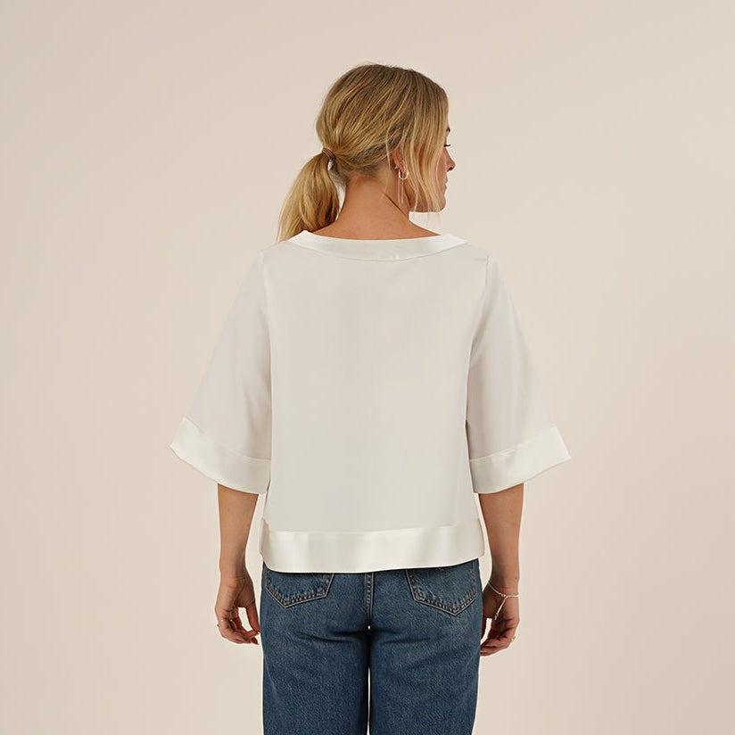 Woman wearing the Silke Blouse sewing pattern in white silk and a pair of Jeans, seen from the back