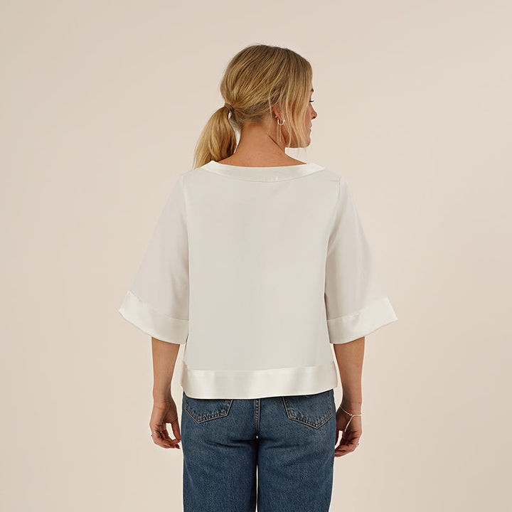 Woman wearing the Silke Blouse sewing pattern in white silk and a pair of Jeans, seen from the back