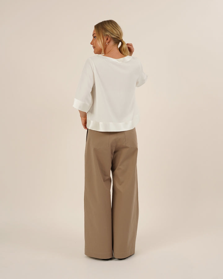 Woman wearing the Silke Blouse sewing pattern in white silk and a pair of Bermuda Pants