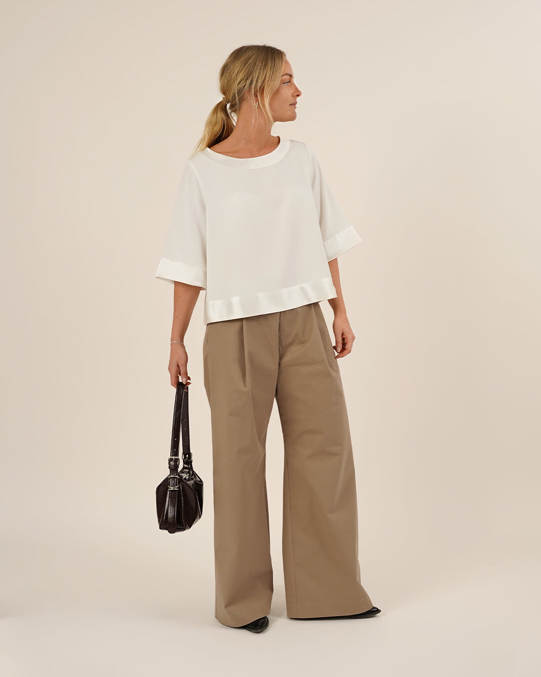 Woman wearing the Silke Blouse sewing pattern in white silk and a pair bermuda pants and a small hand bag