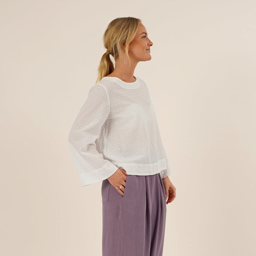 Woman wearing a white Silke blouse sewing pattern and purple Palazzo pants on a beige background