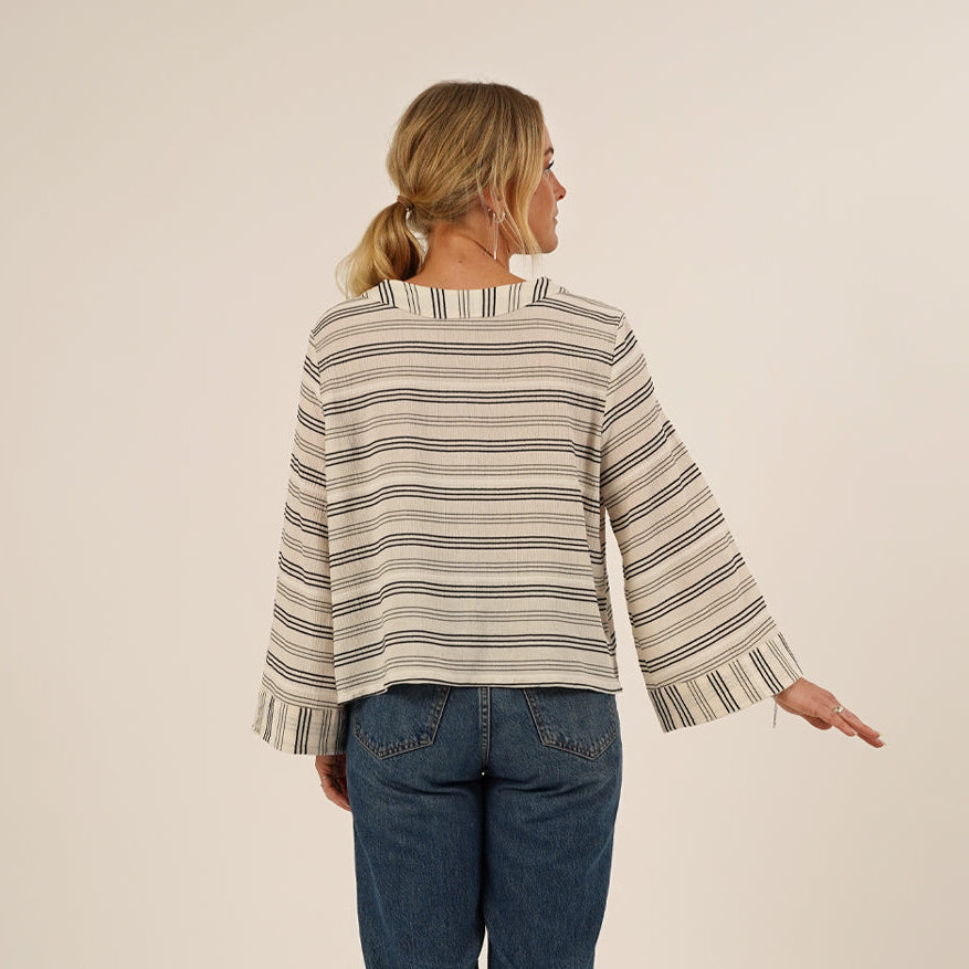 Woman wearing the Silke Blouse sewing pattern seen from the back, and a pair of Jeans