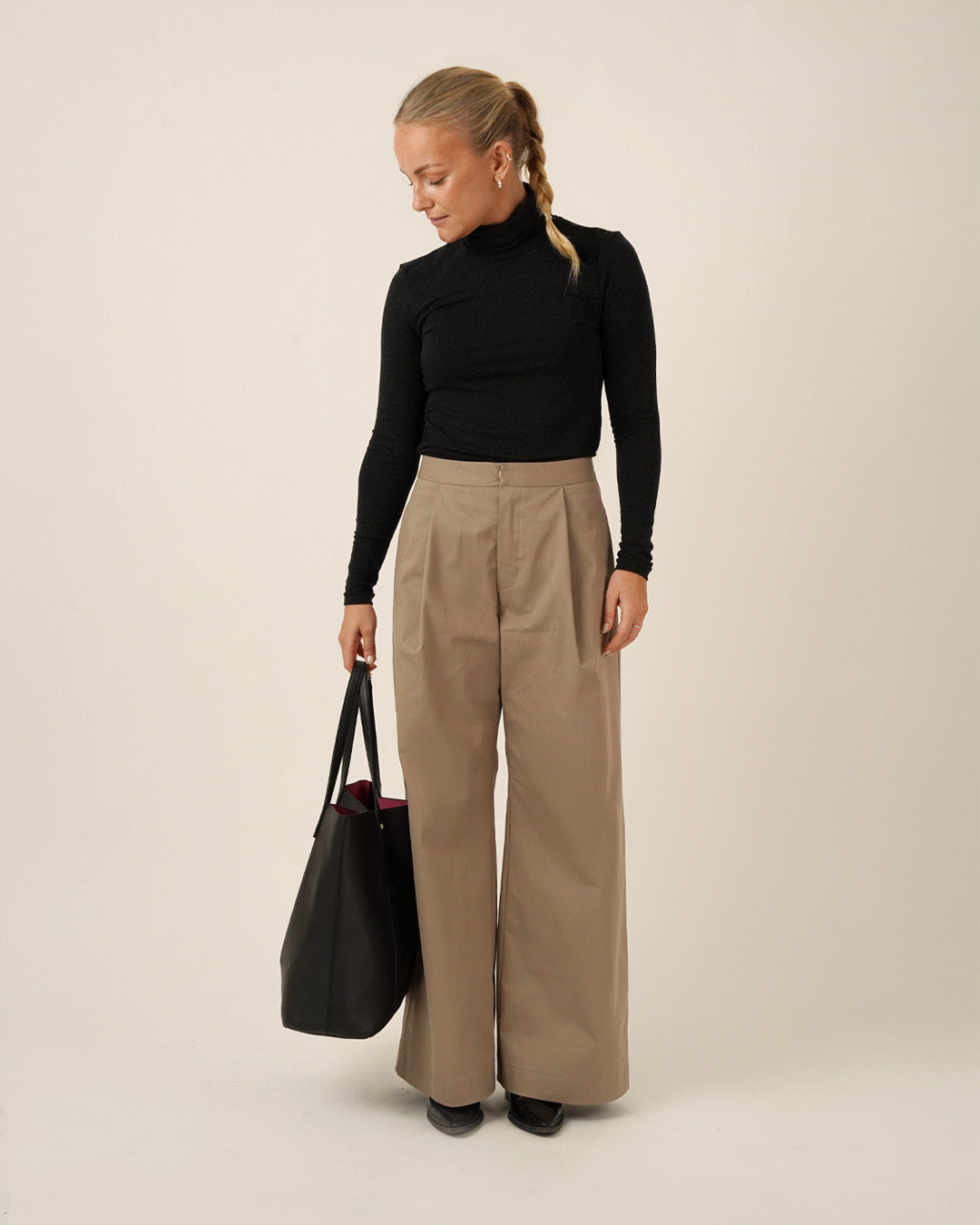 Model wearing high-waisted Bermuda Pants and Shorts Sewing Pattern with a black top and holding a black tote bag.