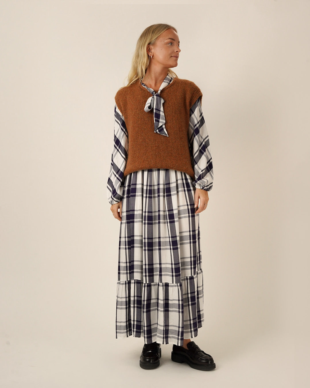 Woman wearing a brown sweater vest over a plaid Freedom dress sewing pattern on a beige background