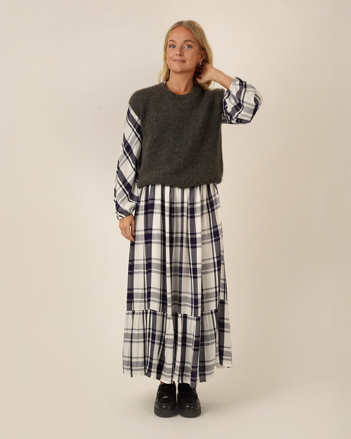 Woman wearing a dark gray sweater and plaid Freedom dress sewing pattern on a plain background