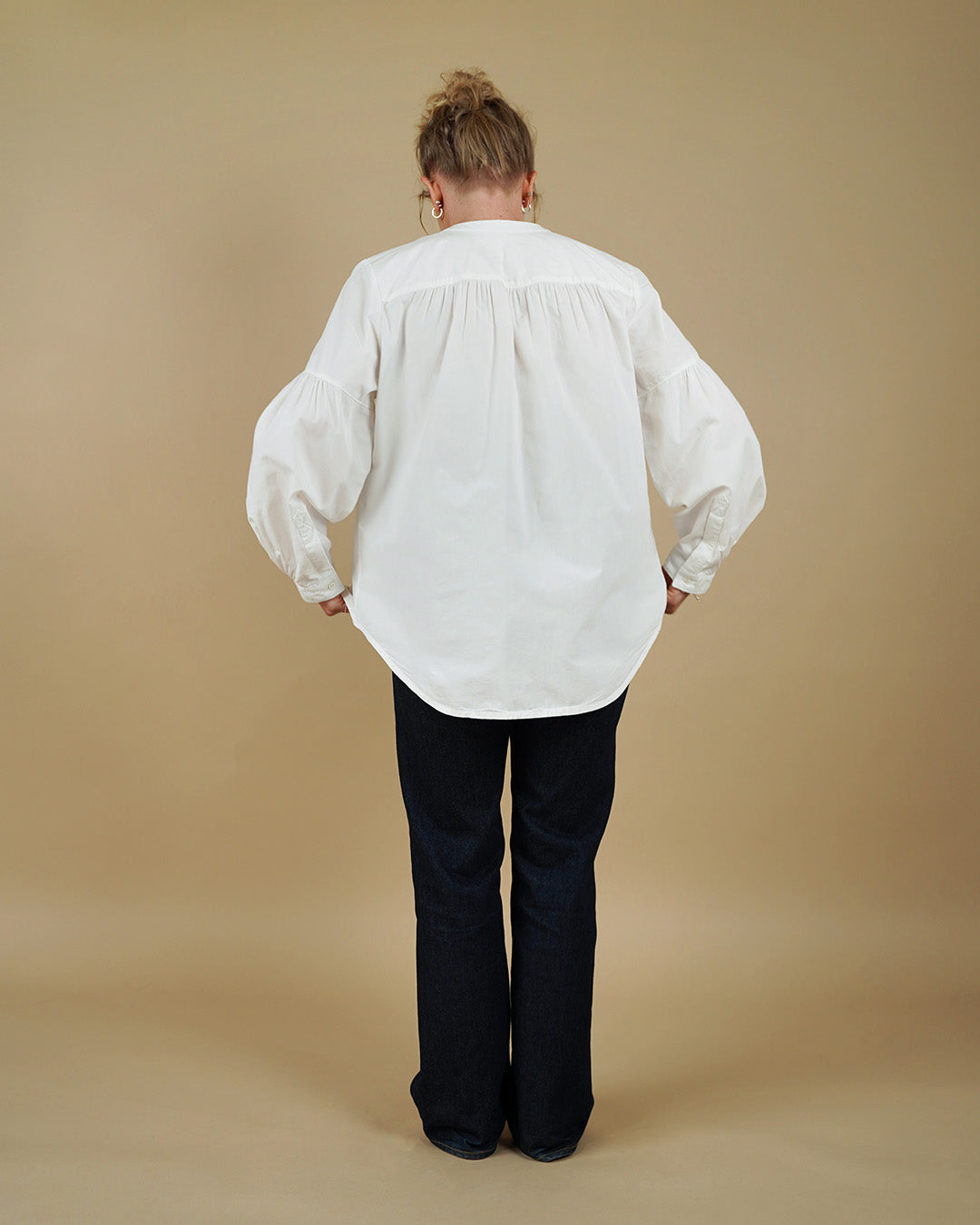 Person wearing a white blouse and black pants against a beige background