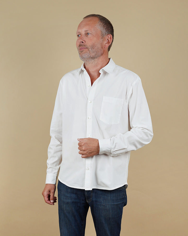 Man wearing a white shirt and dark pants against a beige background