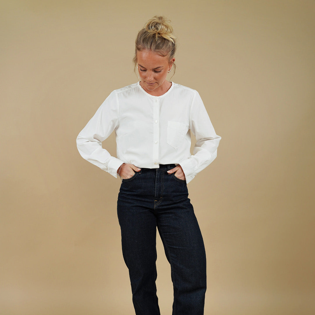 Woman wearing a white blouse and black jeans against a beige background