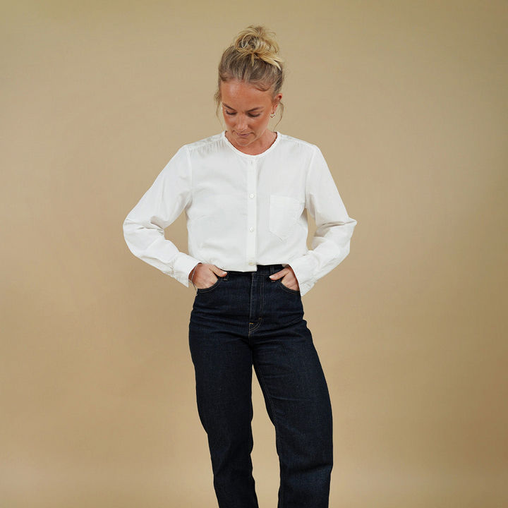Woman wearing a white blouse and black jeans against a beige background