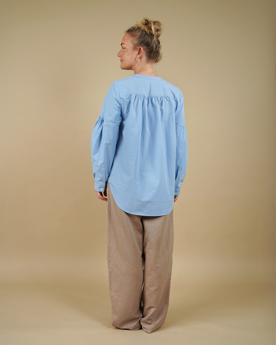 Person wearing a light blue shirt and beige pants against a beige background