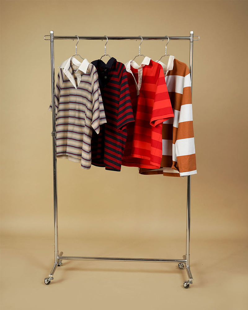 Five short-sleeve polo shirts in various stripe and solid patterns, hanging on a silver metal rolling clothing rack against a solid beige background.