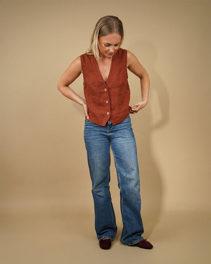 Model wearing a Waistcoat top sewing pattern in rust color with deep V-neck and button closure, paired with blue jeans.