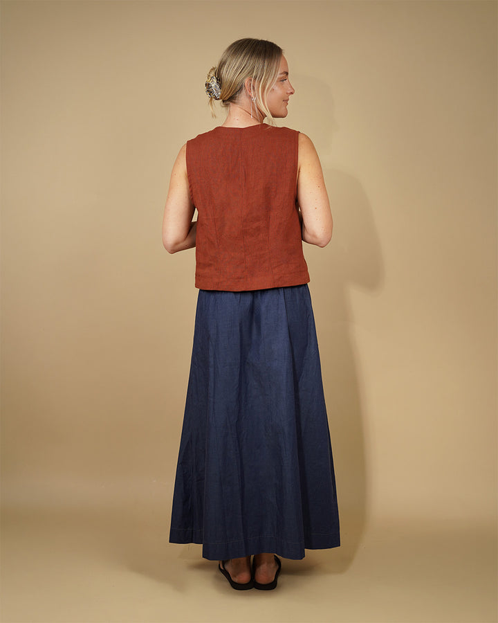 Model wearing a Waistcoat top sewing pattern with a rust-colored top and a long blue skirt from the back.