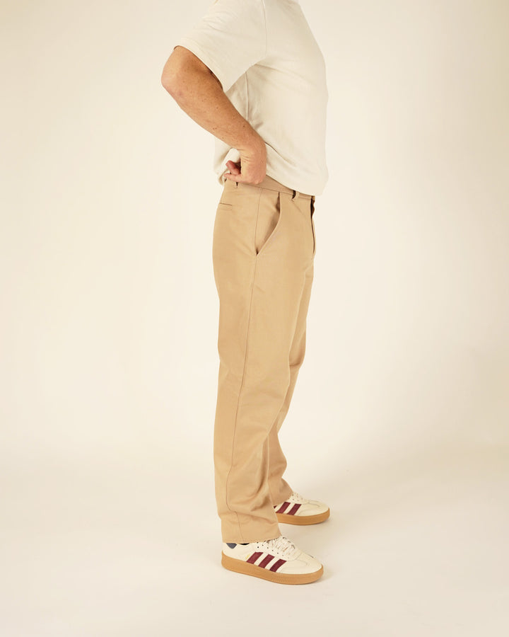 Person wearing beige pants and white sneakers with red stripes on a plain background