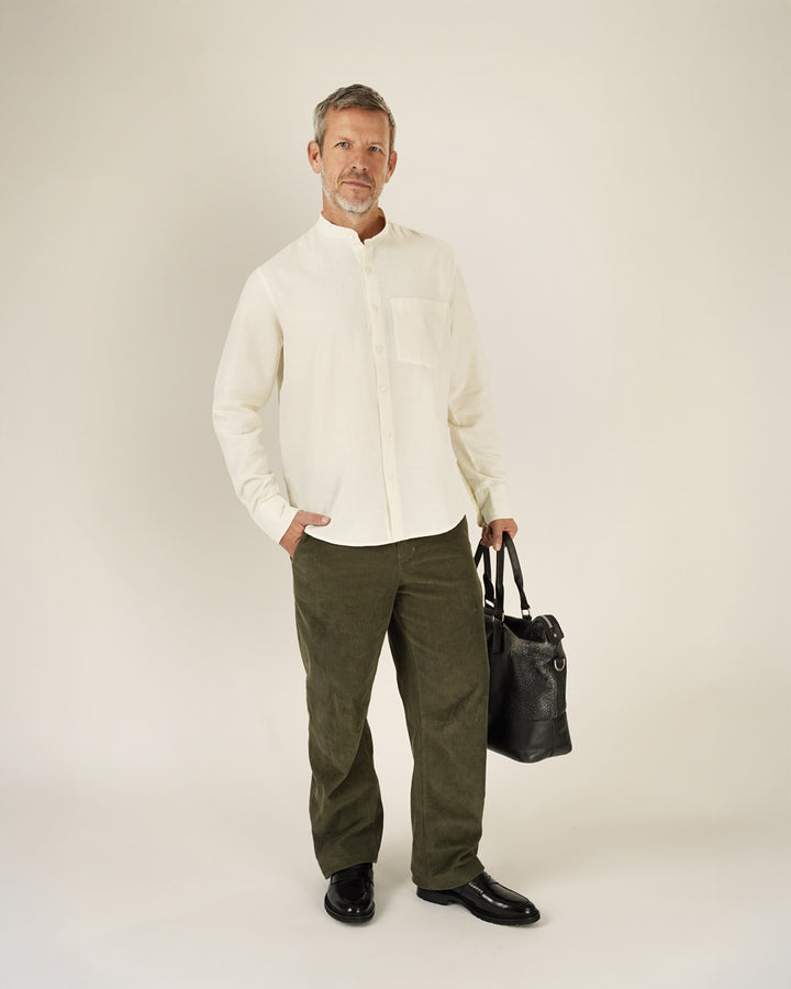 Man wearing a white shirt and green pants holding a black bag on a plain background