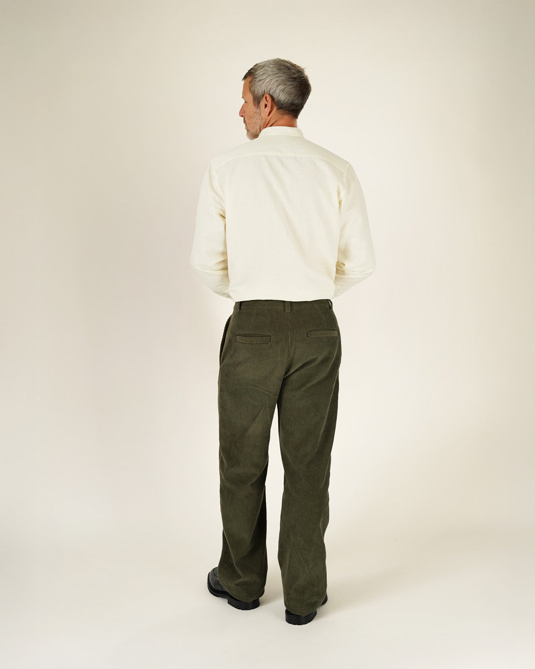 Man wearing a white shirt and green pants on a plain background