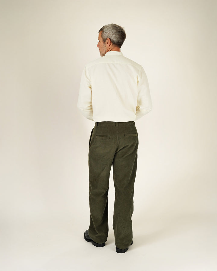 Man wearing a white shirt and green pants on a plain background