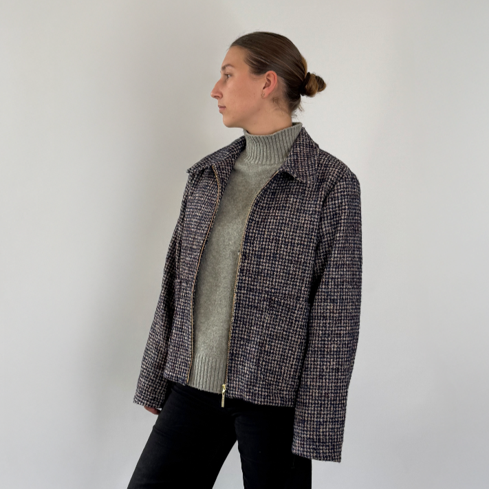Person wearing a checkered jacket over a turtleneck with black pants on a white background