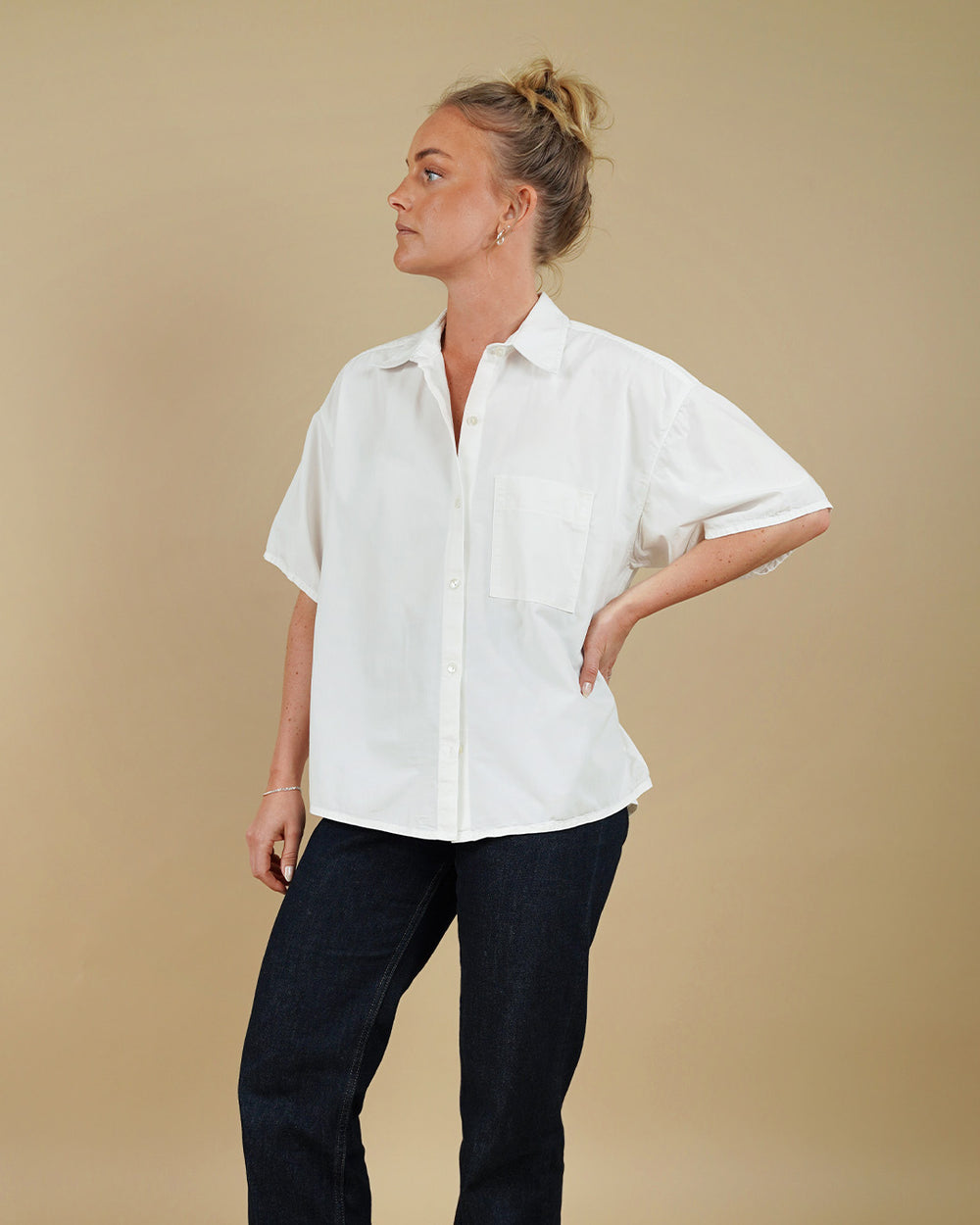 Woman wearing a white shirt and dark pants against a beige background