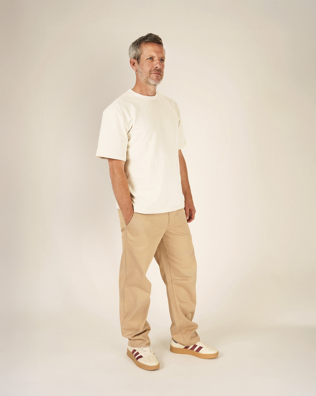 A man wearing a relaxed Big T-shirt sewing pattern in cream color, paired with beige pants and sneakers.