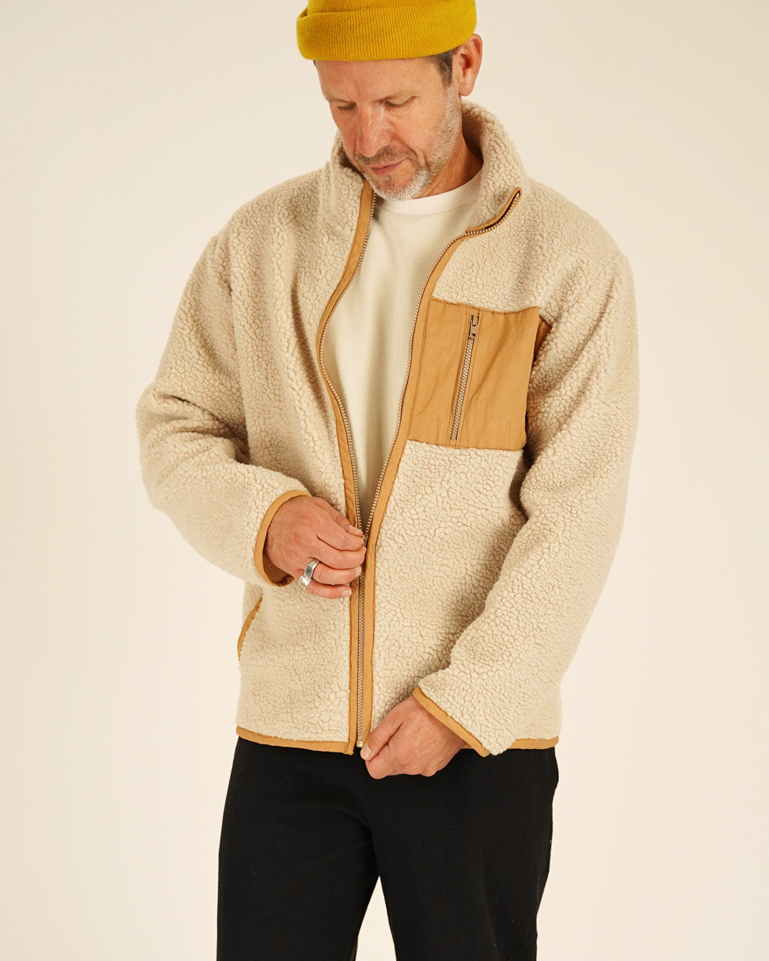 Man wearing a beige and brown fleece jacket on a plain background
