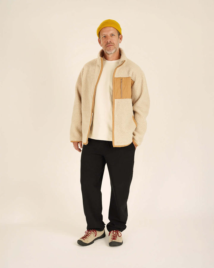 Man wearing a beige jacket with a brown patch, black pants, and a yellow beanie on a white background