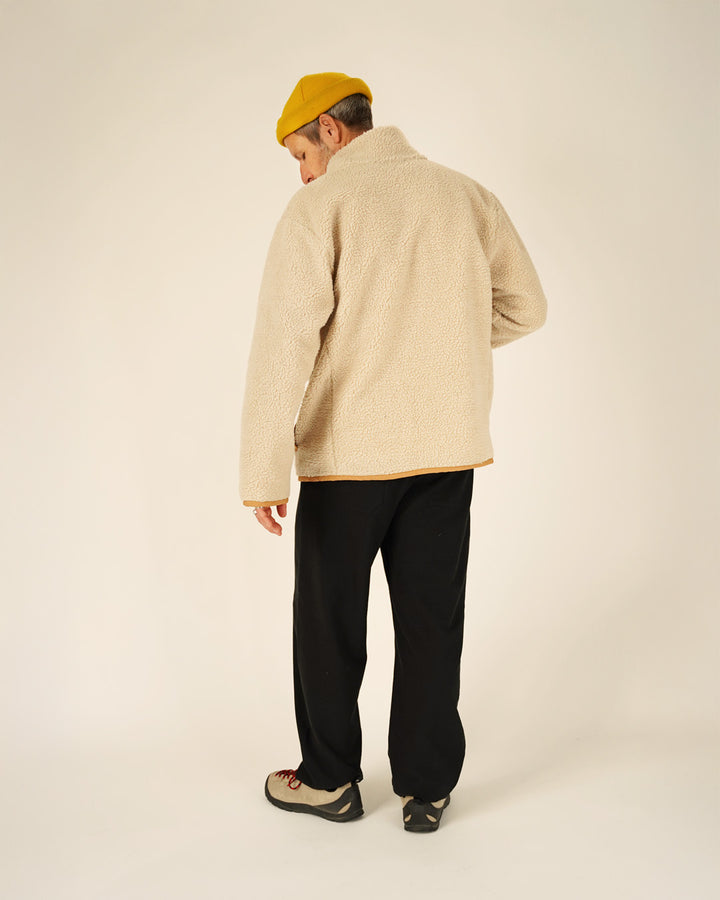 Person wearing a beige jacket and black pants with a yellow hat on a plain background
