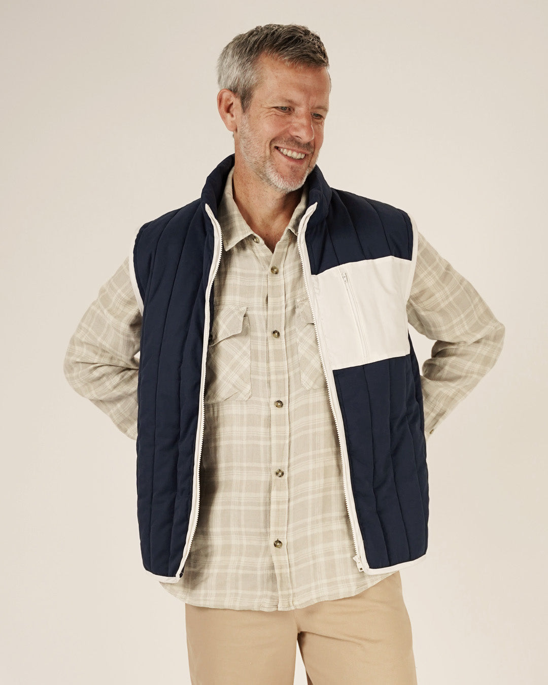 Man wearing a checkered shirt and navy and white quilted vest on a beige background