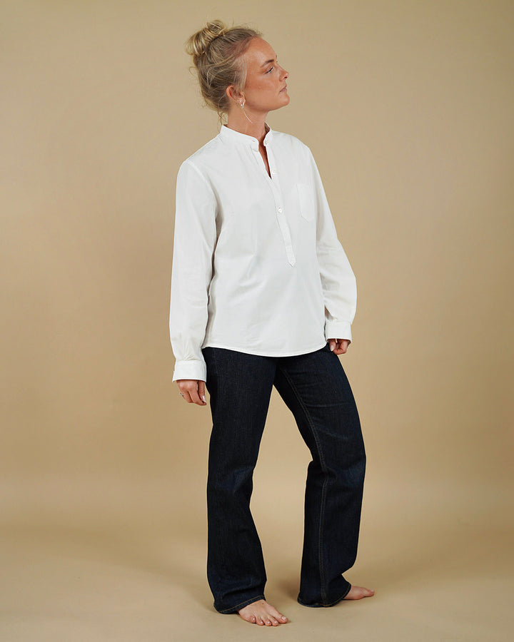 Woman wearing a white tunic and black pants against a beige background