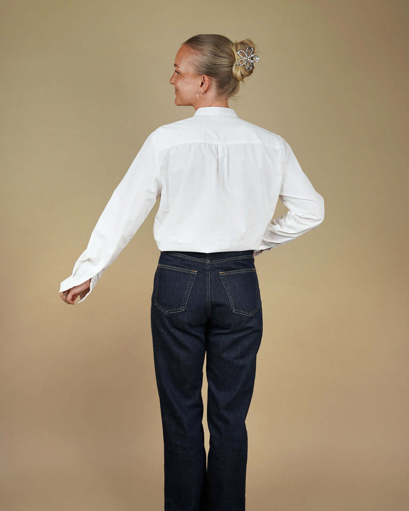 Person wearing a white shirt and dark jeans against a beige background