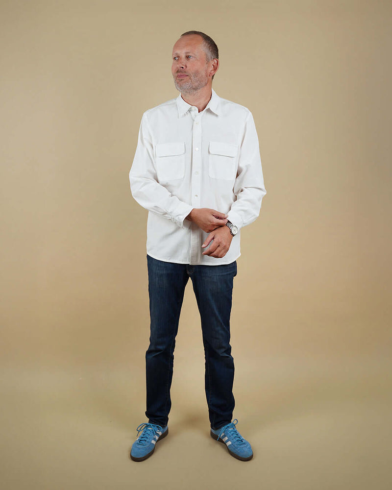 Man wearing a white shirt and blue jeans against a beige background