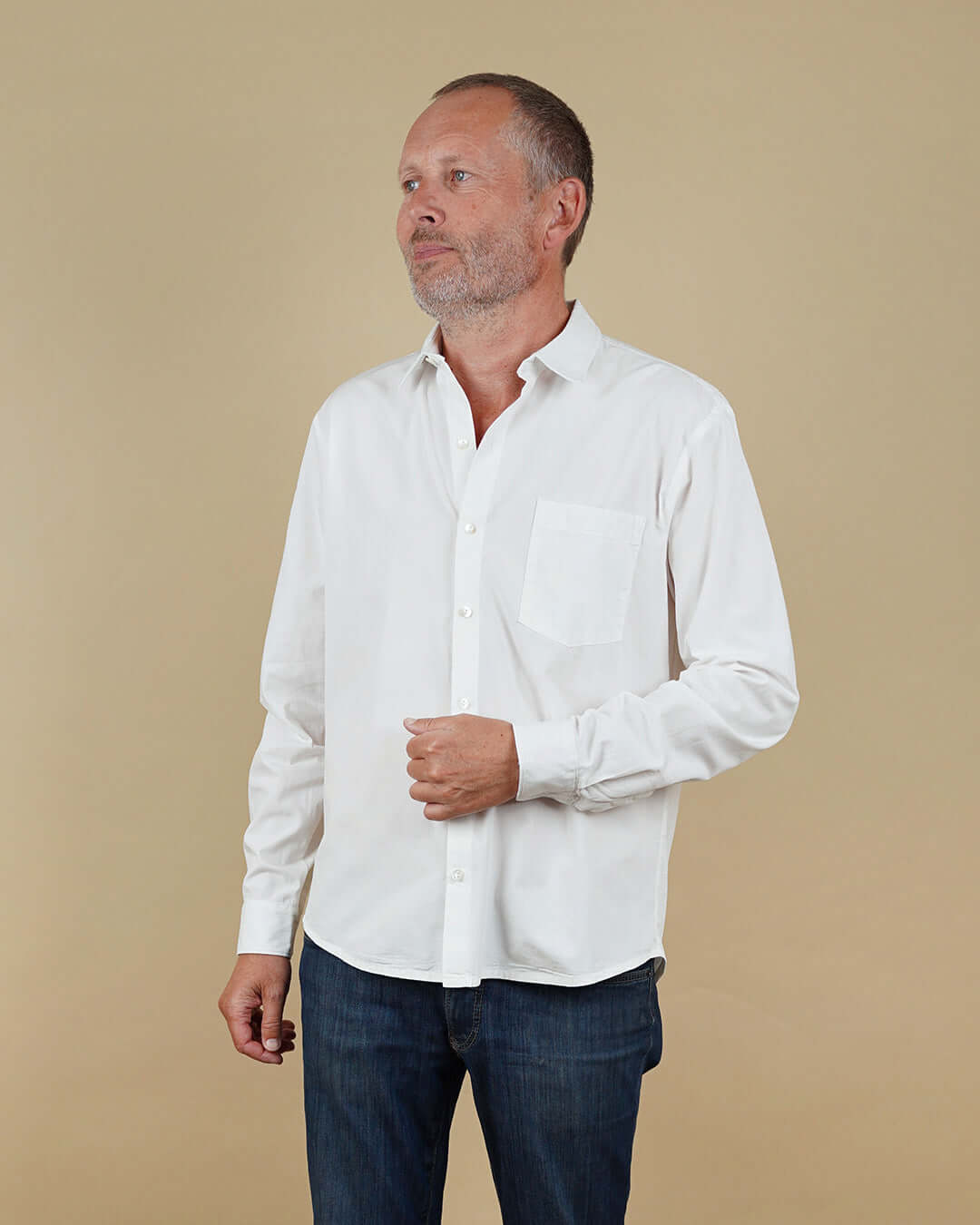 Man wearing a white shirt and dark pants against a beige background